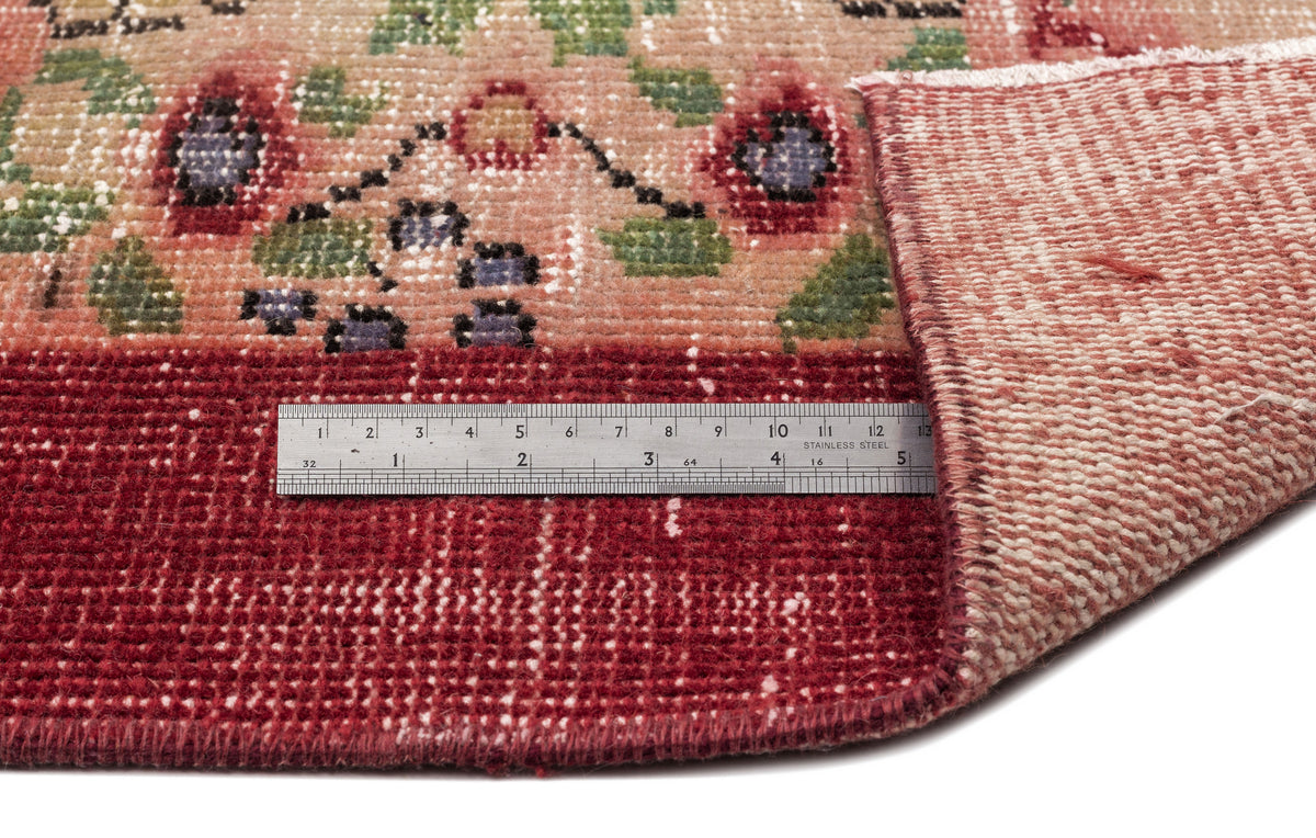 Distressed red and peach floral rug with a folded corner and a metal ruler for scale.