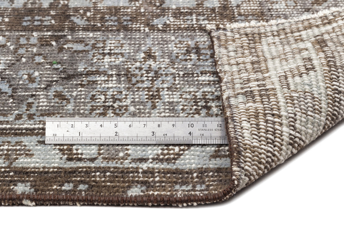 Brown and grey distressed pattern rug with a folded corner and a metal ruler for scale.
