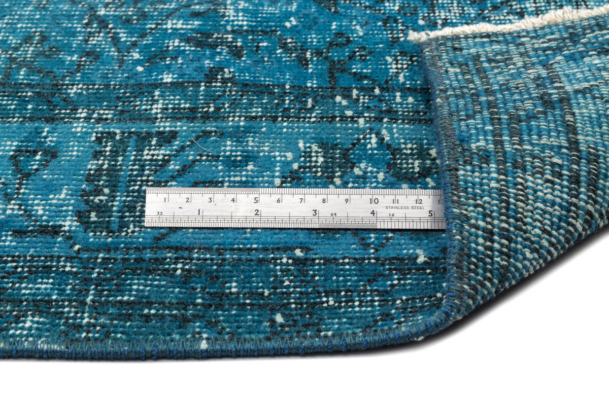 Teal and black distressed traditional rug with a folded corner and a metal ruler for scale on a white background.