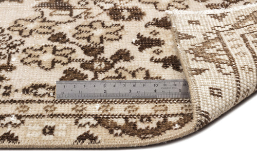 Load image 1 in gallery view. Beige and brown floral medallion rug with a folded corner and a metal ruler for scale.
