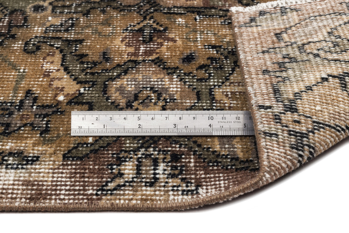 Brown and olive green traditional rug with a distressed floral pattern, shown with a metal ruler for scale.