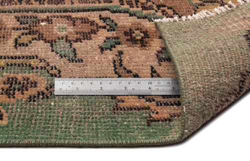 Load image 1 in gallery view. Brown and green vintage-style rug with a floral pattern, showing the underside and a metal ruler for scale.