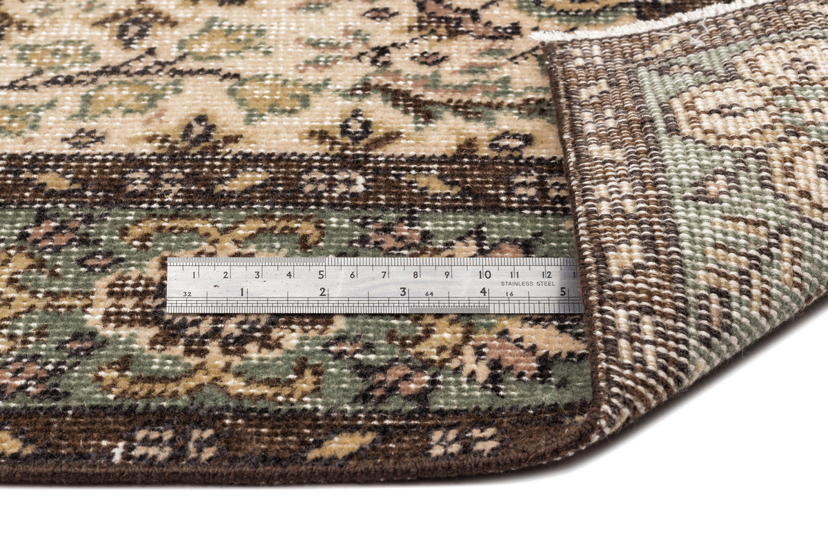 Beige, brown, and sage green traditional floral rug with a folded corner and a metal ruler for scale.