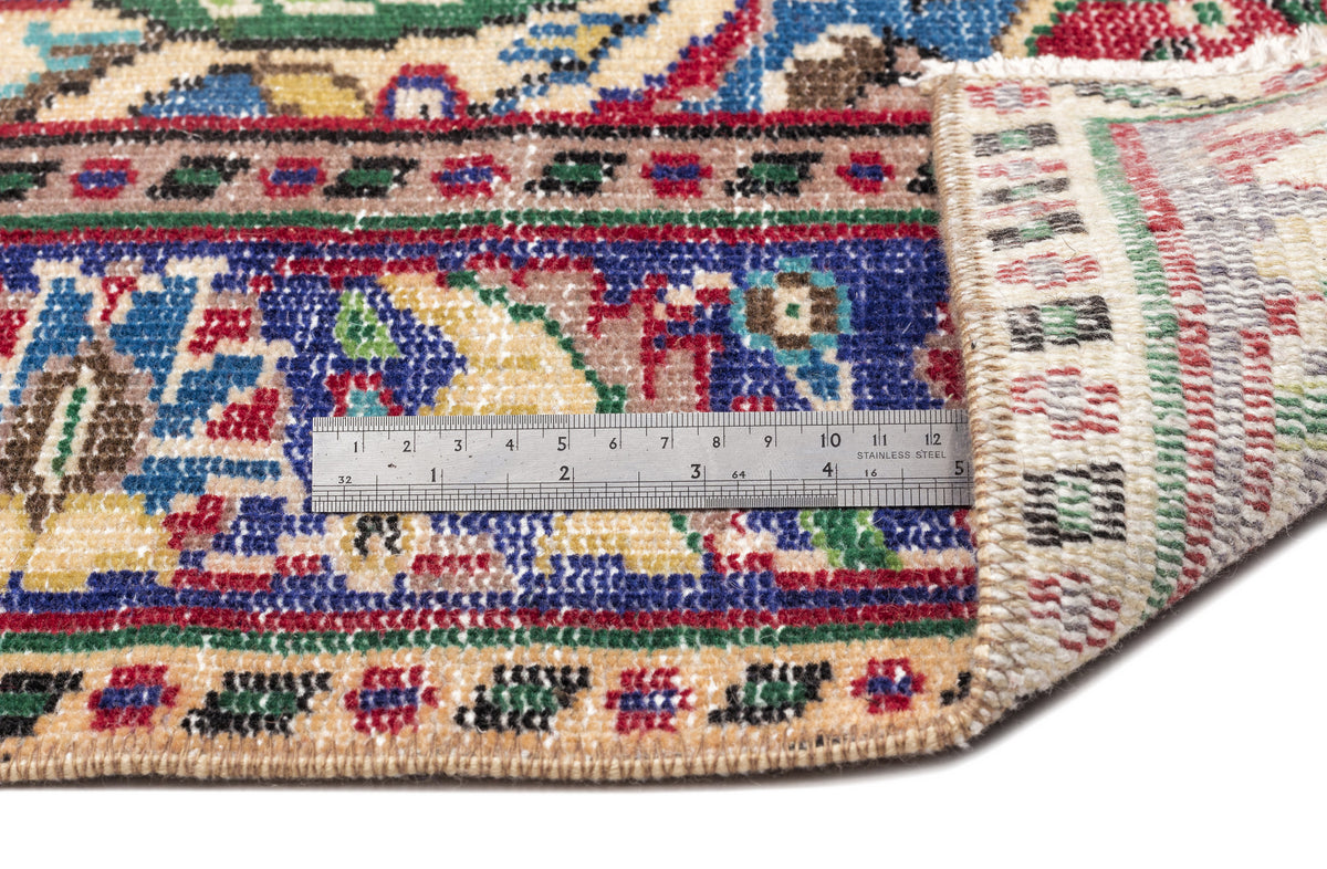 Multi-colored traditional Persian-style rug with a folded corner and a metal ruler for scale on a white background.
