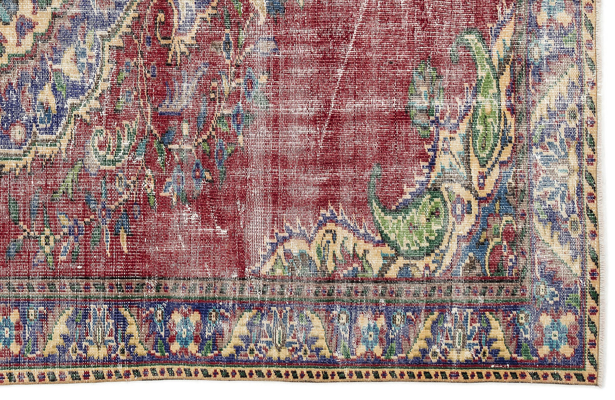 Distressed red, blue, and green vintage-style rug with a traditional floral medallion pattern and a fringed border.