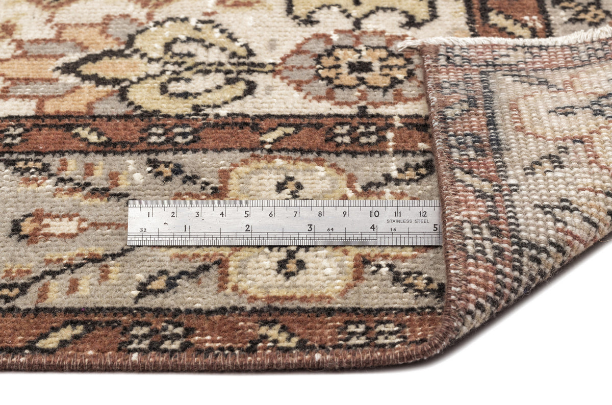 Beige, brown, and grey traditional rug with a floral medallion pattern, shown with a metal ruler for scale.