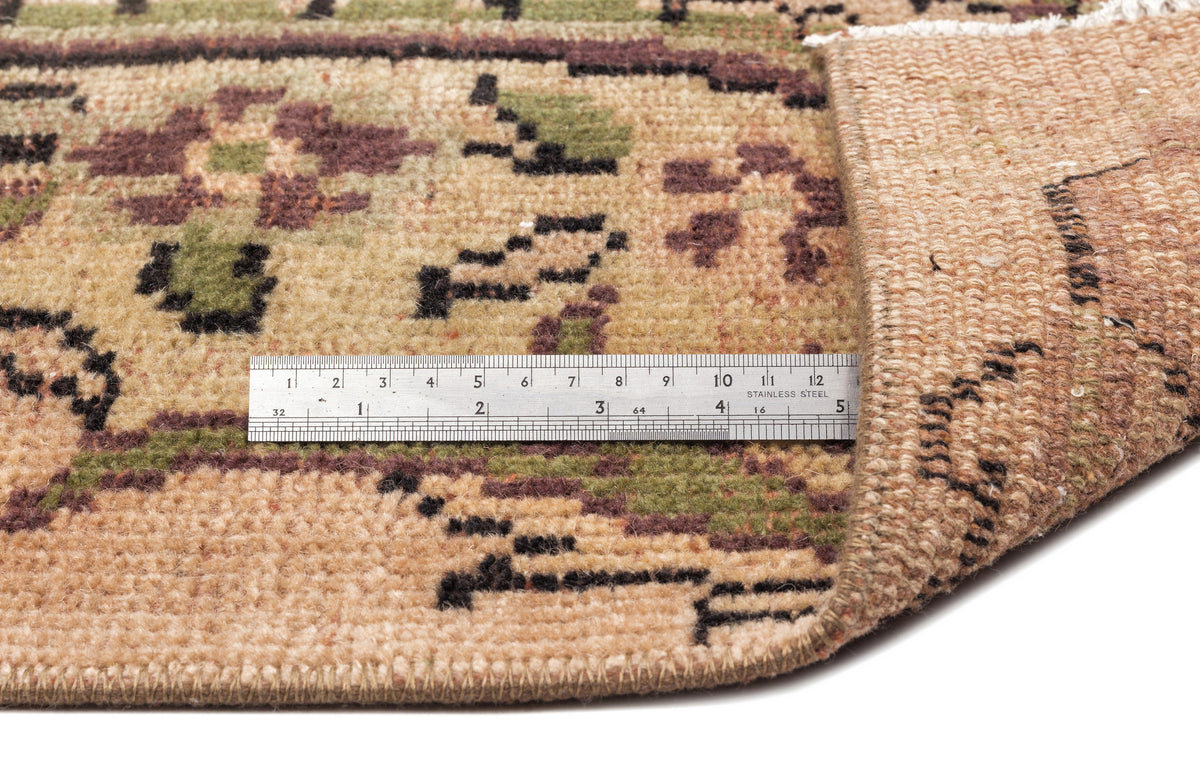 Tan, green, and brown floral patterned rug with a folded corner and a metal ruler for scale.