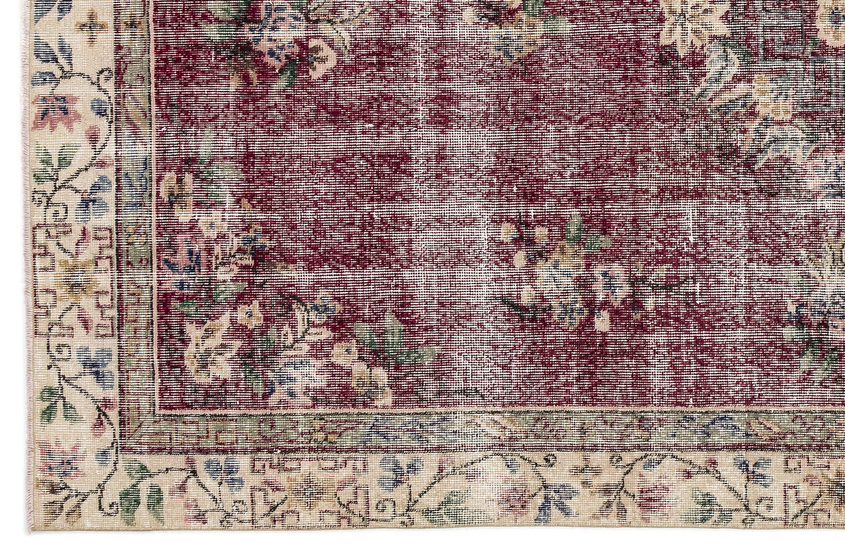 Distressed burgundy rug with a floral pattern and a cream border featuring intricate botanical motifs.