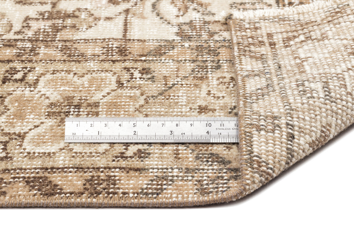 Beige and brown distressed traditional rug with a folded corner and a metal ruler for scale on a white background.