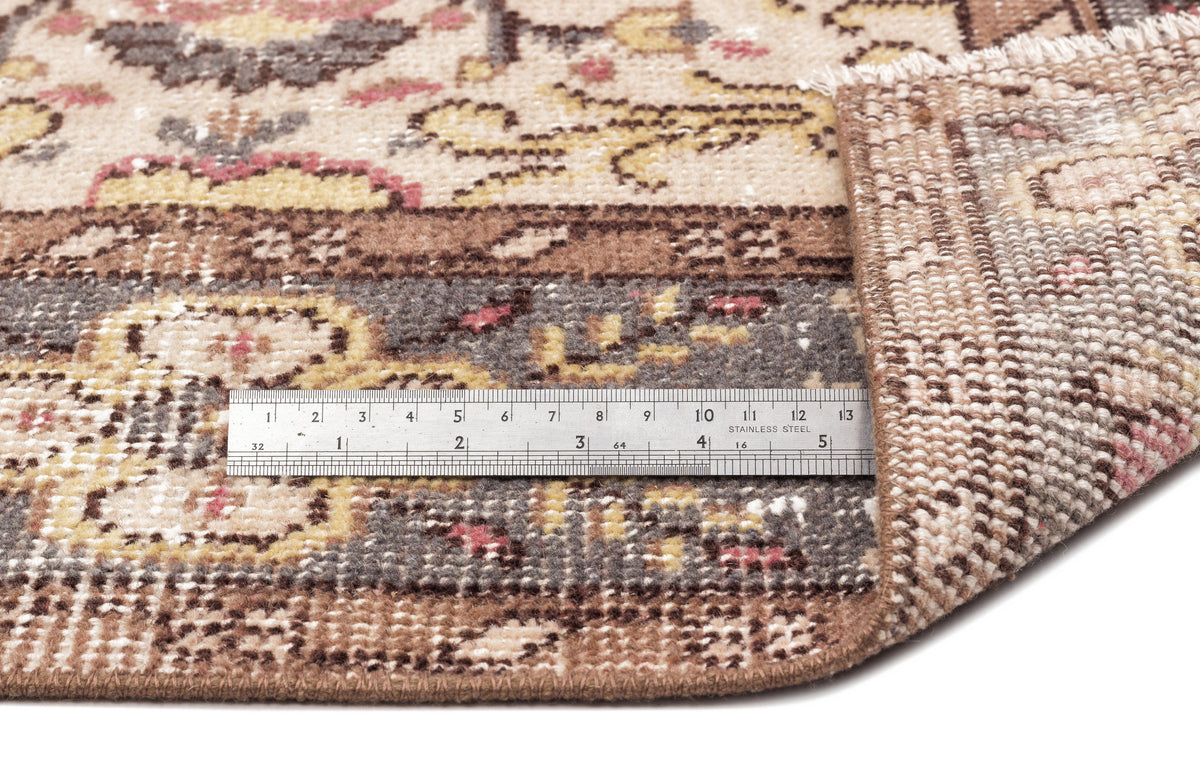 Beige, brown, and muted pink traditional rug with a floral medallion pattern, shown with a metal ruler for scale.