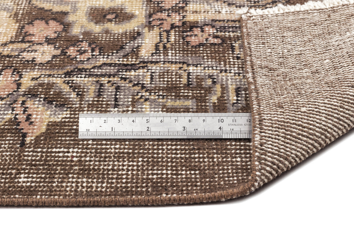 Brown and beige vintage-style rug with a floral medallion pattern, shown with a metal ruler for scale.
