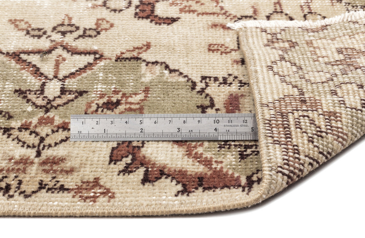 A metal ruler shows inches and centimeters on the Clera - Vintage Medallion Rug (5'7 x 8'10); one corner is folded to reveal the underside and detailed edge stitching.