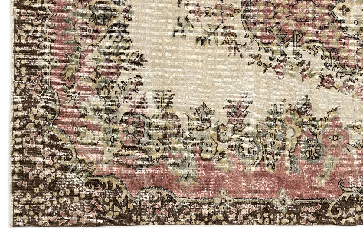 Distressed traditional rug with a floral medallion pattern in muted pink, sage green, and brown on a cream background.