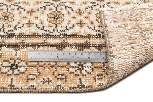 Load image 1 in gallery view. Tan and cream rug with a dark brown floral medallion pattern, shown folded to reveal the woven backing and a metal ruler.
