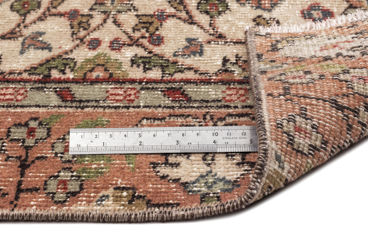 Beige, terracotta, and green traditional floral rug with a folded corner and a metal ruler for scale.