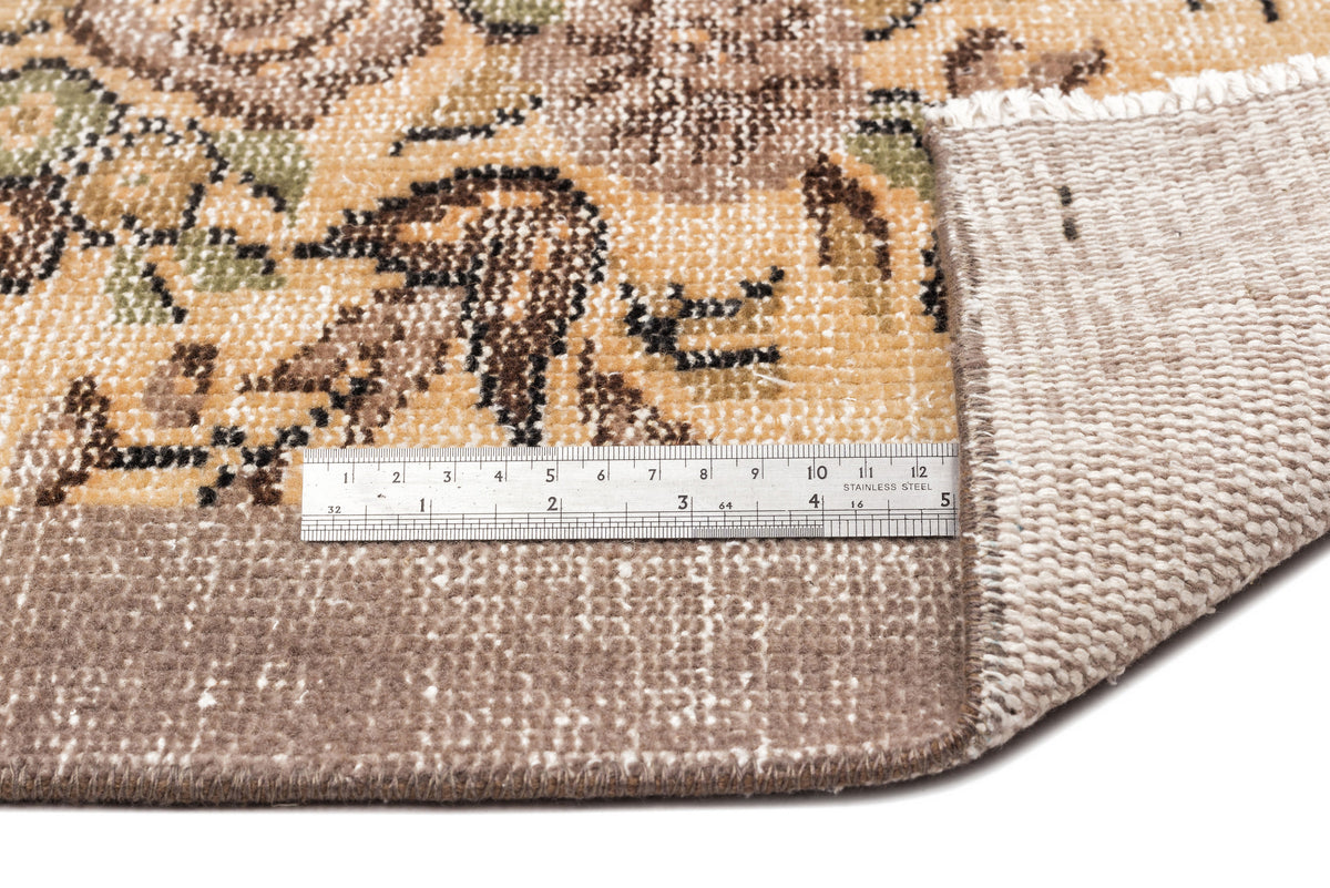 Tan, brown, and green floral patterned rug with a folded corner and a stainless steel ruler for scale.