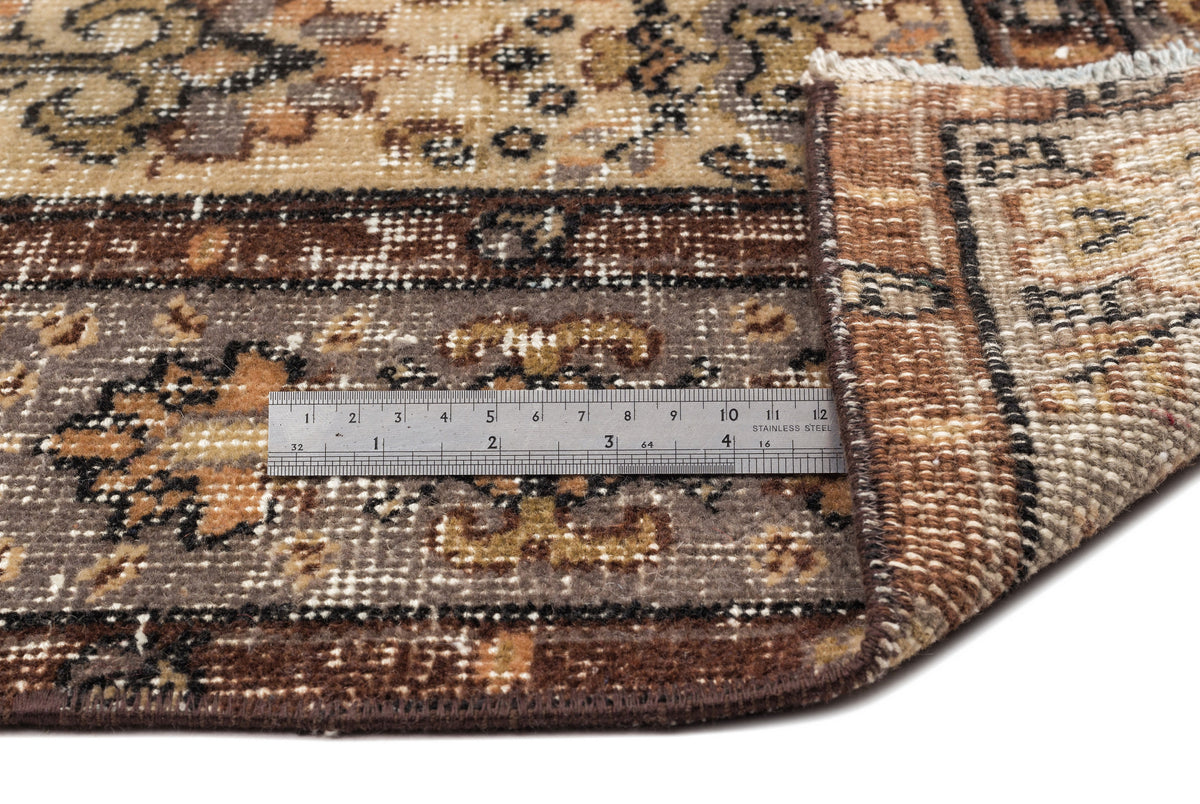 Brown, tan, and grey vintage-style rug with a traditional floral medallion pattern and a metal ruler for scale.