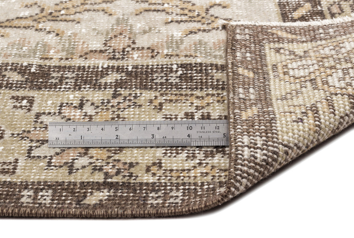 A close-up of the Sadeane - Vintage Floral Rug (6'0 x 9'8) shows its flatwoven corner folded to reveal the underside, with a metal ruler beside it displaying inch and centimeter measurements for scale.