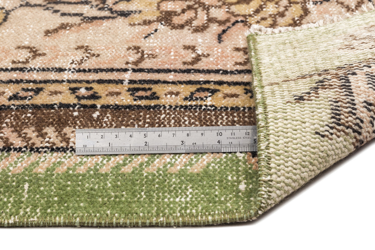 Beige, brown, and green vintage-style rug with a floral pattern, shown with a metal ruler for scale.