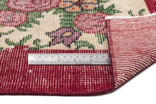 Load image 1 in gallery view. Cream rug with floral pattern in red, green, and purple, featuring a red border and a metal ruler for scale.