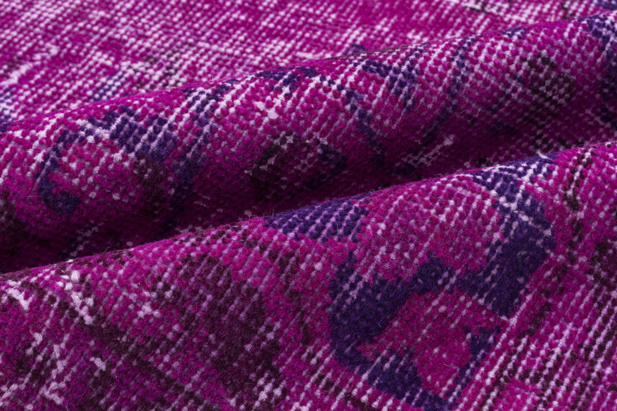 Close-up of a magenta and deep purple distressed rug with a faded traditional pattern and visible fabric texture.