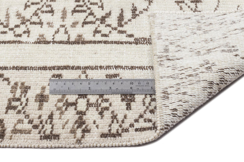 Load image 1 in gallery view. A metal ruler rests on the Greunoa - Vintage Floral Rug - 5'4 X 9'6, which features a folded corner to highlight its thickness and detailed cream and brown patterned texture.
