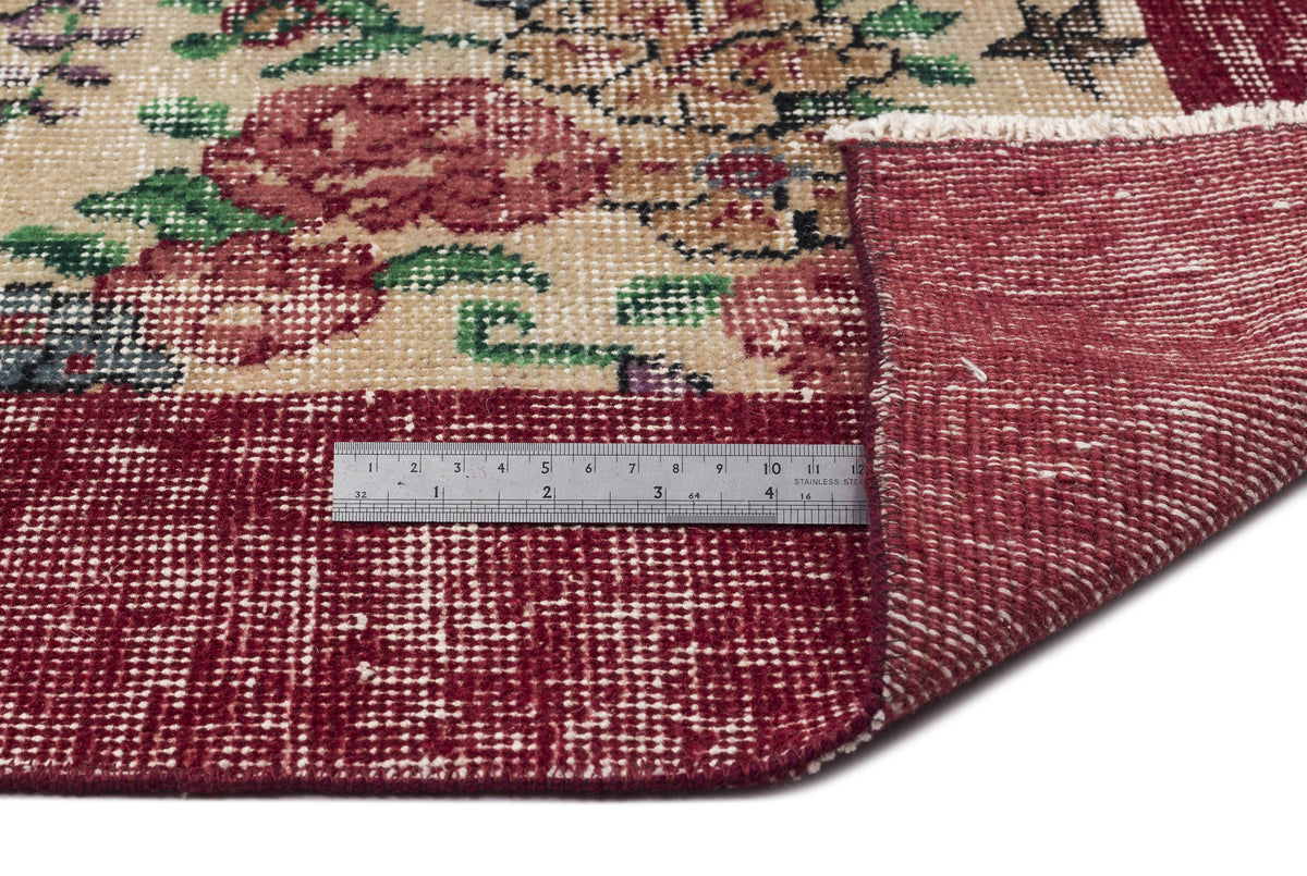Beige and red floral rug with a folded corner revealing the underside, shown with a metal ruler for scale.