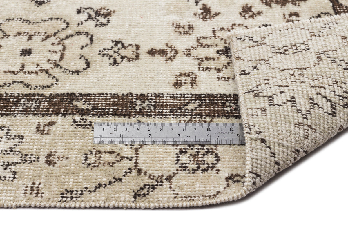 Cream and brown distressed floral pattern rug with a folded corner and a metal ruler for scale.