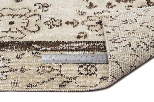Load image 1 in gallery view. Cream and brown distressed floral pattern rug with a folded corner and a metal ruler for scale.