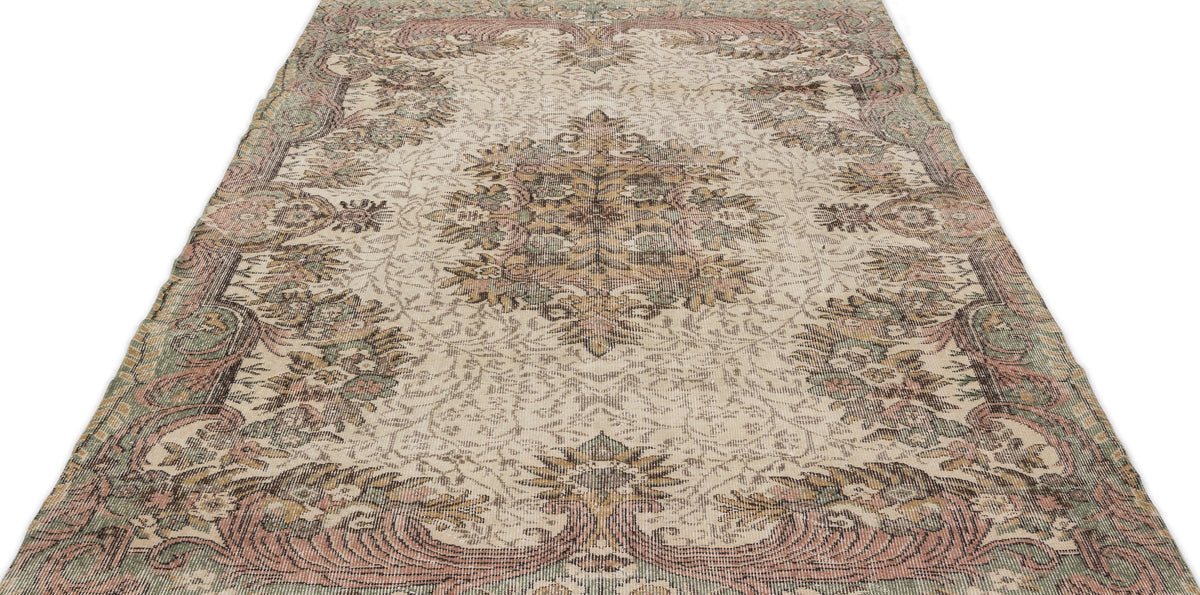 Beige vintage-style rug with a distressed floral medallion pattern in muted pink, sage green, and brown tones.