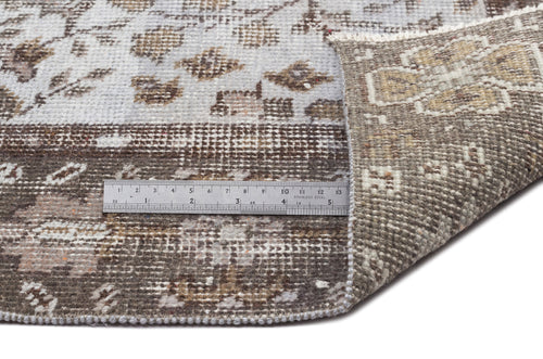 Load image 1 in gallery view. Brown and grey distressed floral rug with a folded corner and a metal ruler for scale on a white background.