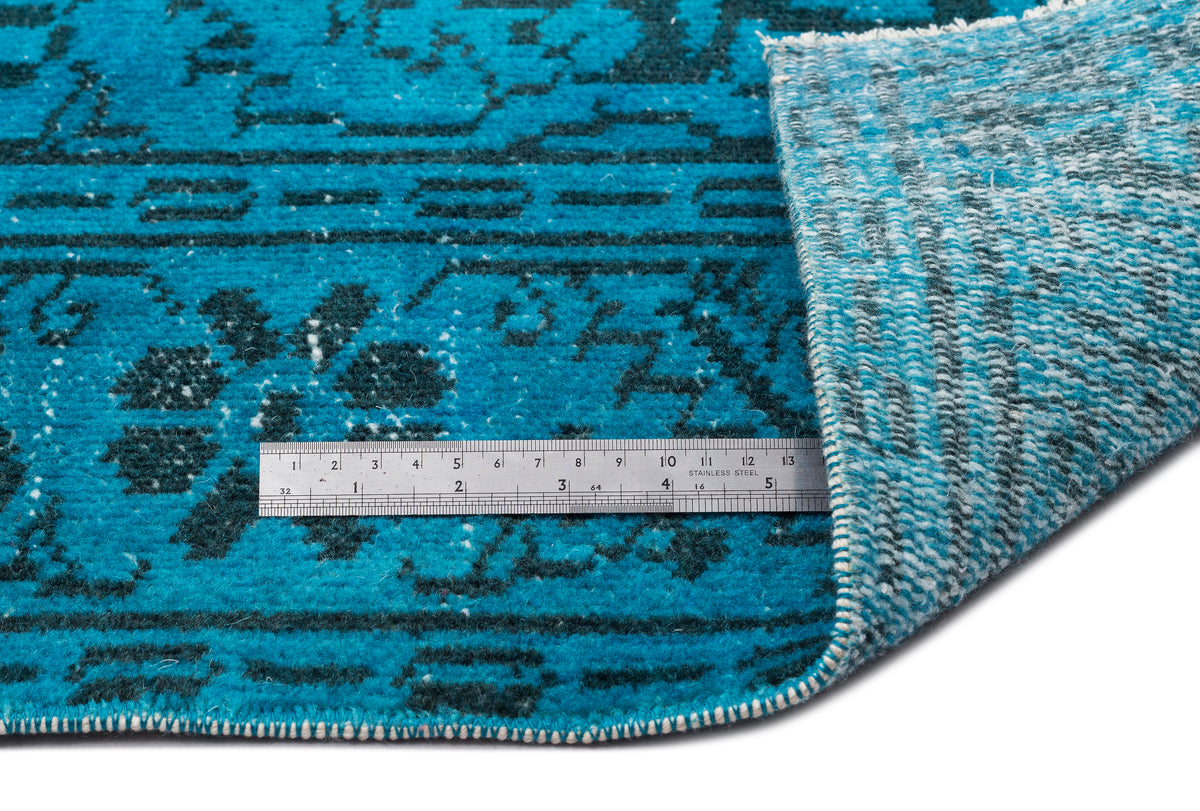 Bright turquoise and dark teal rug with a traditional floral pattern, showing the pile and backing with a metal ruler.