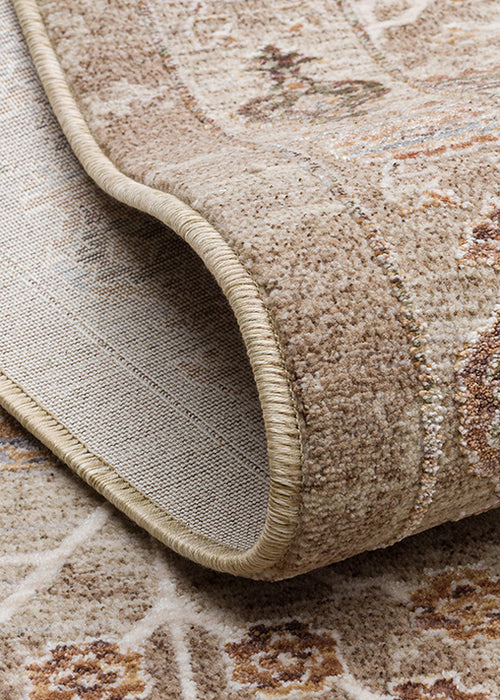 Load image 1 in gallery view. Beige and tan traditional rug with a folded corner showing the woven backing and stitched edge.