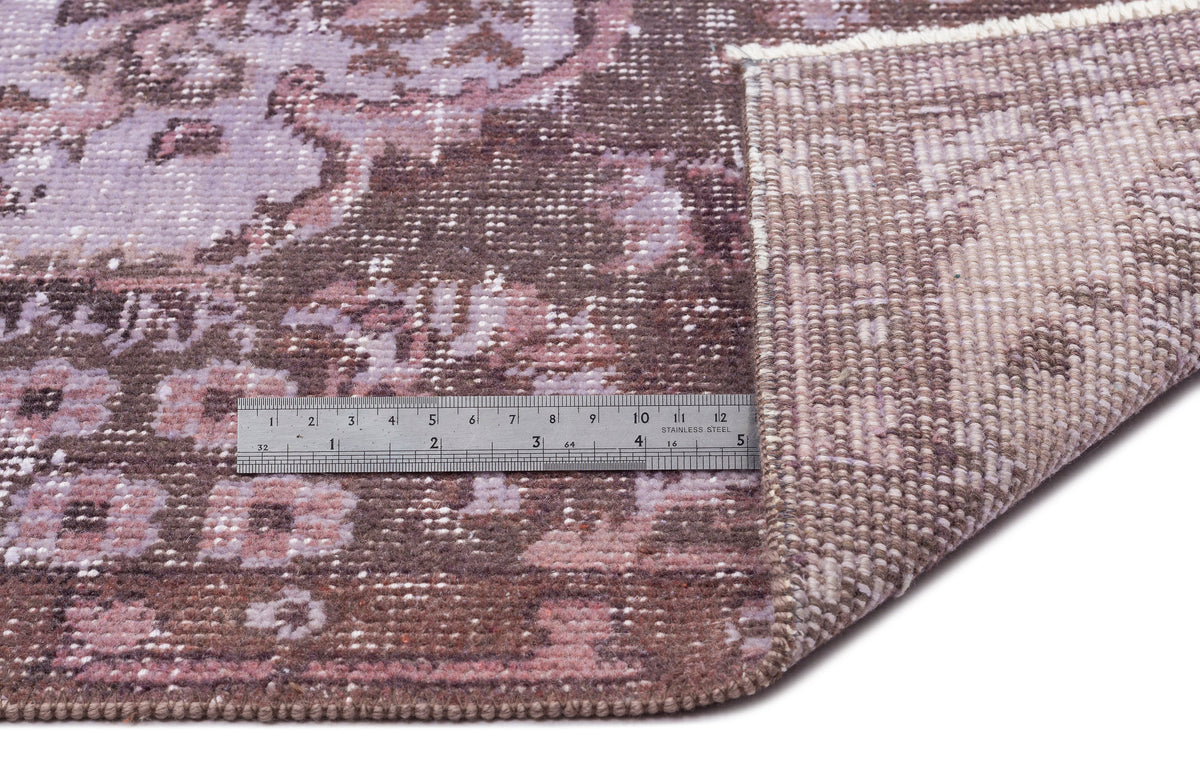 Distressed mauve and brown rug with a traditional floral medallion pattern, shown with a metal ruler for scale.