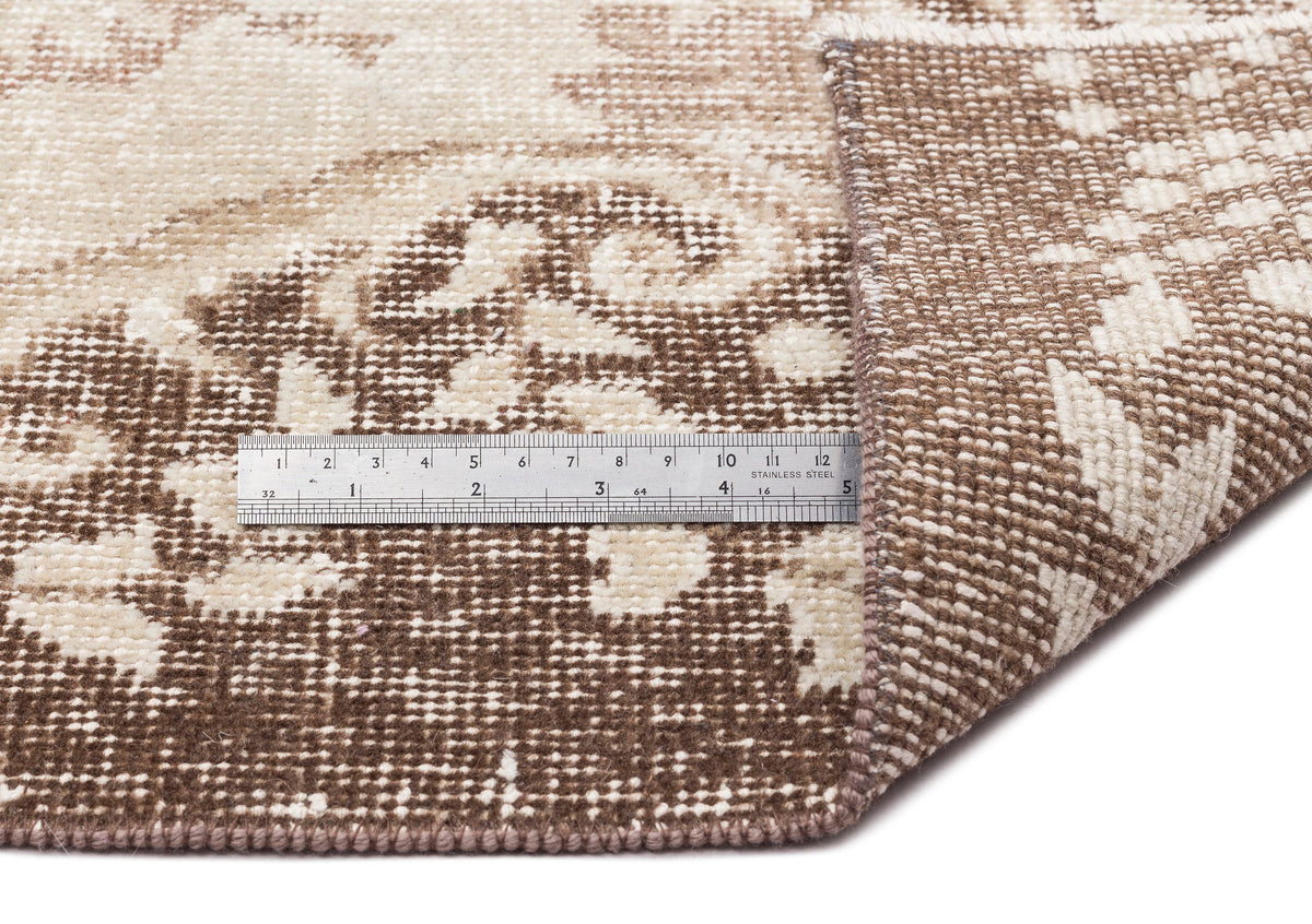 A close-up of the Pririna Vintage Medallion Rug (6'2" x 9'7"), showing its brown and cream pattern with one corner folded over and a metal ruler on top measuring about 6 inches.