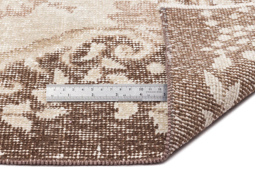 Load image 1 in gallery view. A close-up of the Pririna Vintage Medallion Rug (6'2" x 9'7"), showing its brown and cream pattern with one corner folded over and a metal ruler on top measuring about 6 inches.
