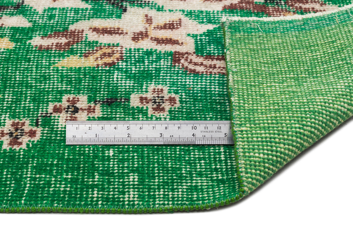 Emerald green rug with a floral medallion pattern in cream and brown, showing the woven backing and a metal ruler.