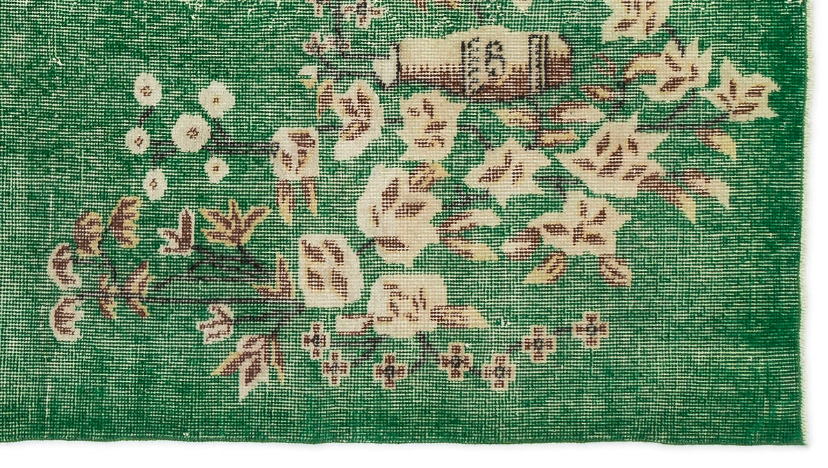 Emerald green rug with a distressed floral pattern in cream and brown, featuring a woven texture.