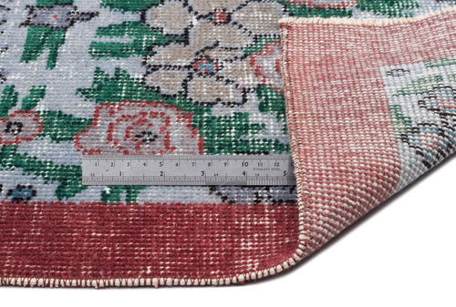 Load image 1 in gallery view. Distressed floral rug in blue, green, and red with a folded corner and a metal ruler for scale on a white background.