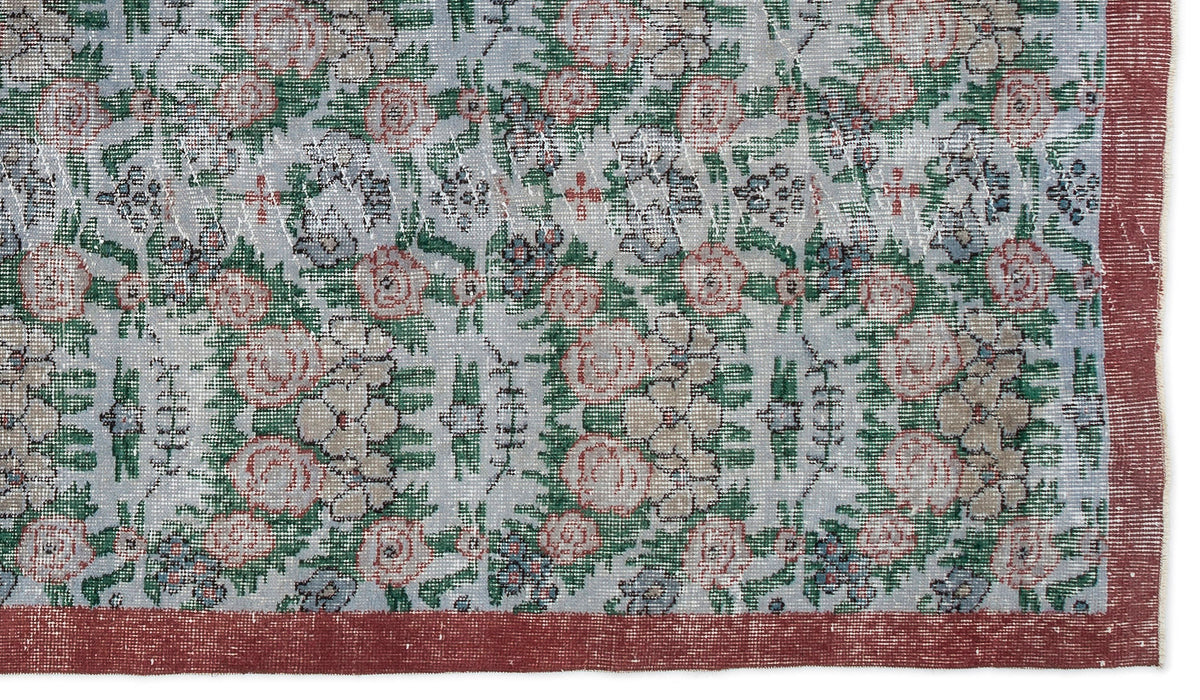Distressed light blue rug with a repeating floral pattern in pink, green, and grey, featuring a solid dark red border.