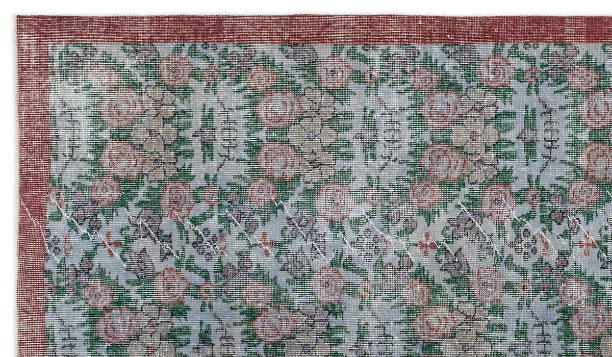 Distressed light blue rug with a floral pattern in red and green, featuring a solid red border.