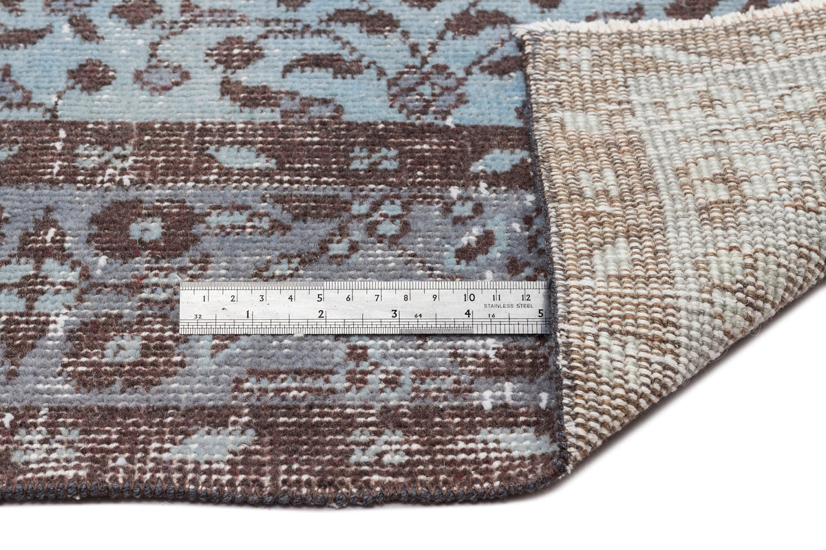 Blue and brown floral patterned rug with a folded corner showing the backing and a metal ruler for scale.