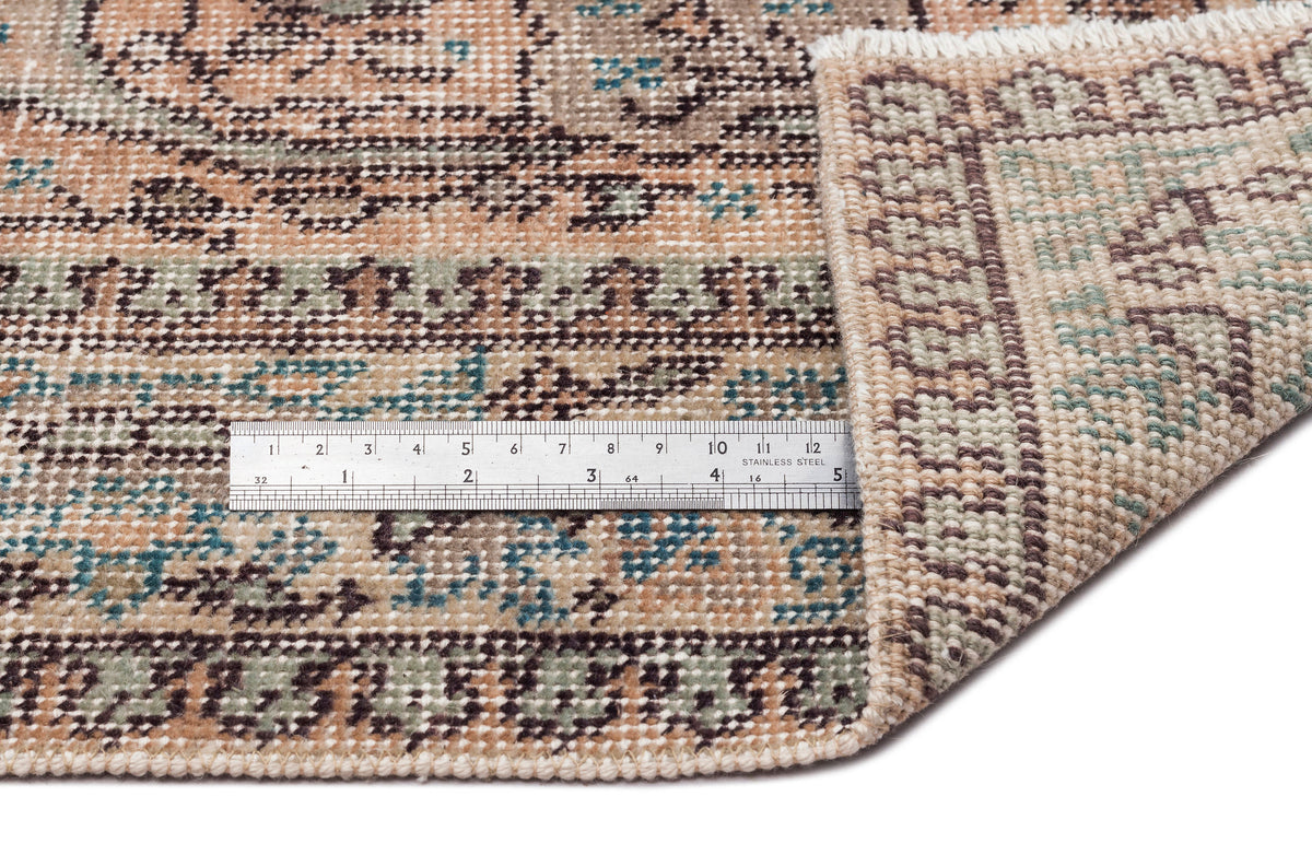 Beige, brown, and teal vintage-style rug with a floral medallion pattern, shown with a metal ruler for scale.