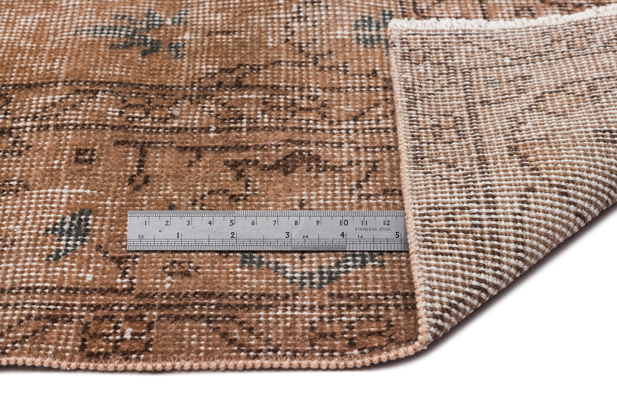Brown and tan distressed vintage-style rug with a folded corner and a metal ruler for scale.
