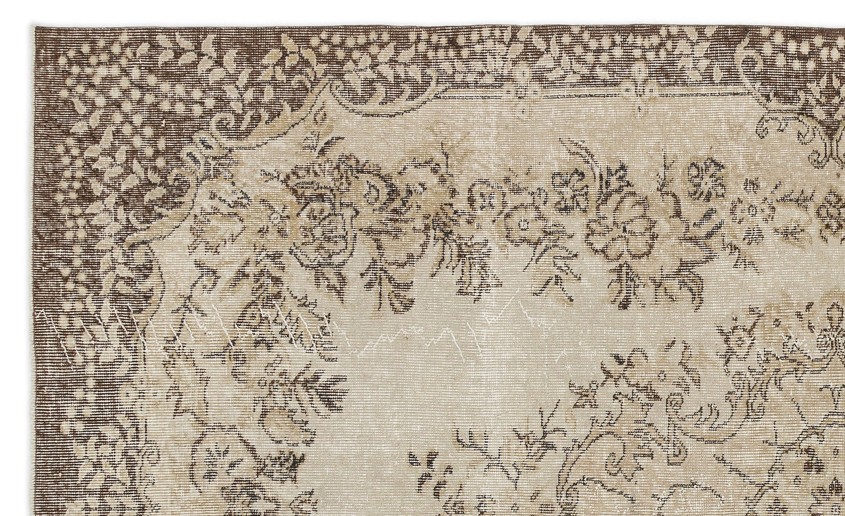 A section of the Petida - Vintage Medallion Rug (5'8 x 9'5) shows a beige background, brown floral motifs, and intricate borders. This vintage rug features a beautifully faded, distressed look.