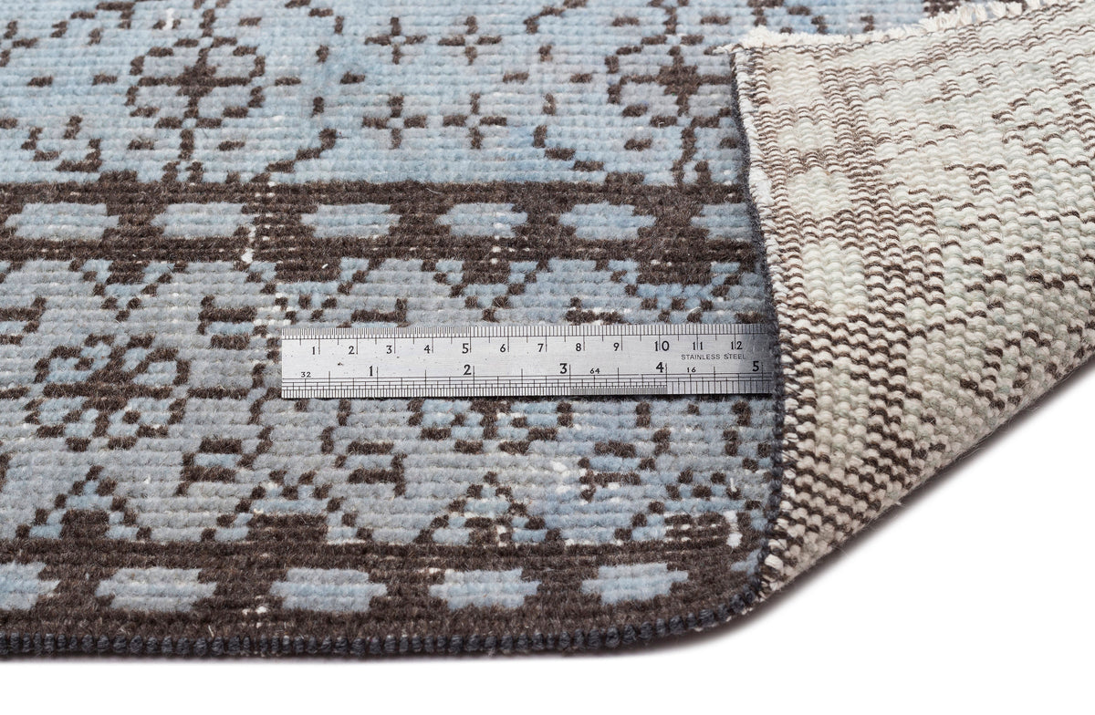 Light blue and dark brown rug with a geometric pattern, shown with a metal ruler for scale and a folded corner.