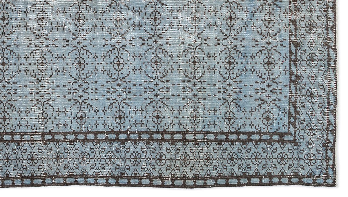 Light blue distressed rug with a dark brown repeating floral medallion pattern and a geometric border.
