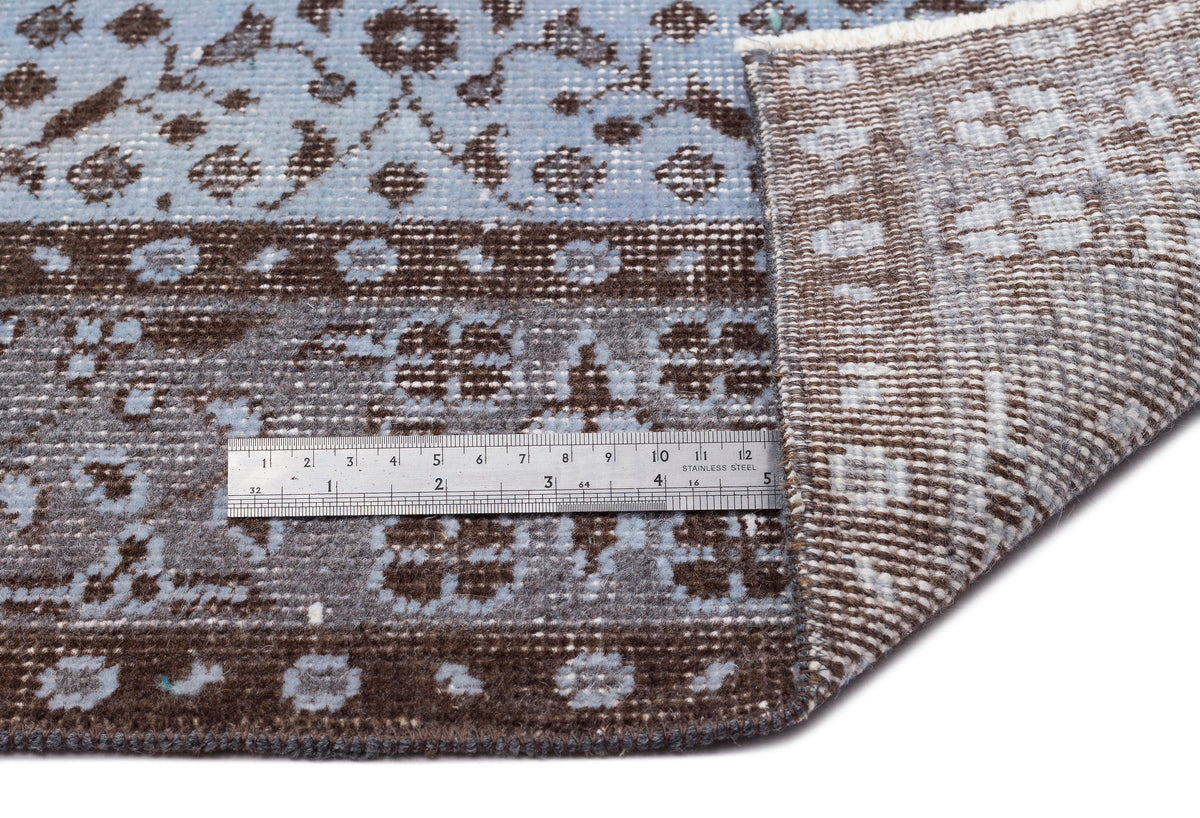 Blue and brown floral patterned rug with a folded corner showing the woven backing and a metal ruler for scale.