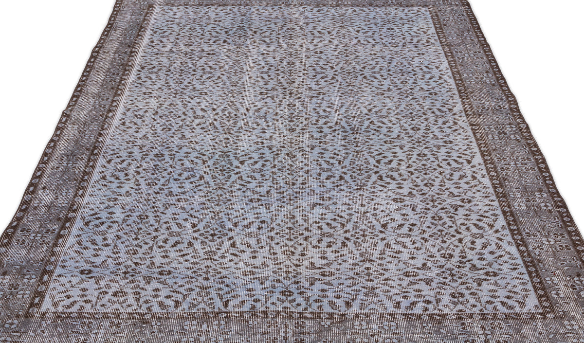 Blue and brown distressed rug with an all-over intricate floral pattern and a wide decorative border.