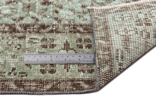 Load image 1 in gallery view. Sage green and brown distressed traditional rug with a folded corner and a metal ruler for scale.